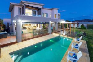 A large pool with chairs around it and a house in the background.